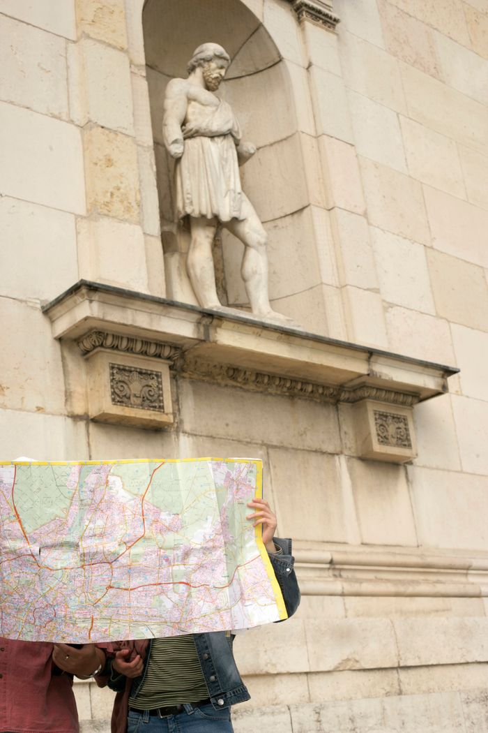 Two travelers holding a map in front of an ancient stone statue on a city tour.