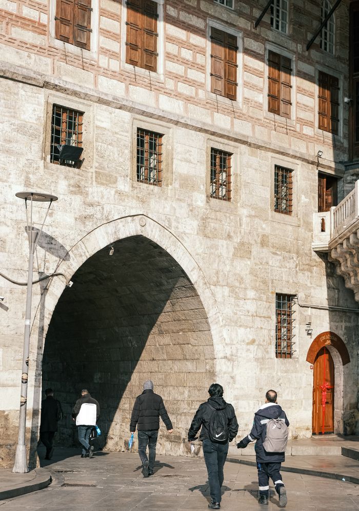 Tourists walk through a historic stone archway on a sunny day, showcasing architectural charm.