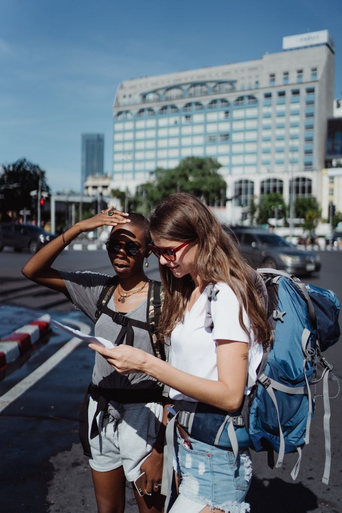 Two young women using a map as they explore a city in the summer sun.